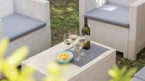 Un coin salon extérieur en osier, agrémenté de coussins, avec une bouteille de vin, des verres à vin et un bol de collations.
