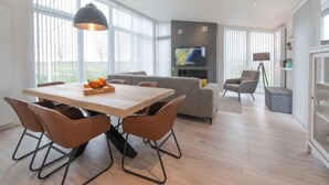 Un salon moderne avec une table à manger en bois, des chaises marron, un canapé gris et un téléviseur à écran plat fixé au mur.