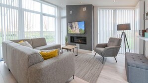 Un salon moderne avec un canapé gris, une table basse, un téléviseur fixé au mur et un lampadaire.