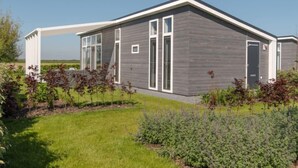 Une maison moderne de plain-pied, avec une façade grise et des éléments décoratifs blancs, entourée d’un jardin bien entretenu et sous un ciel dégagé.