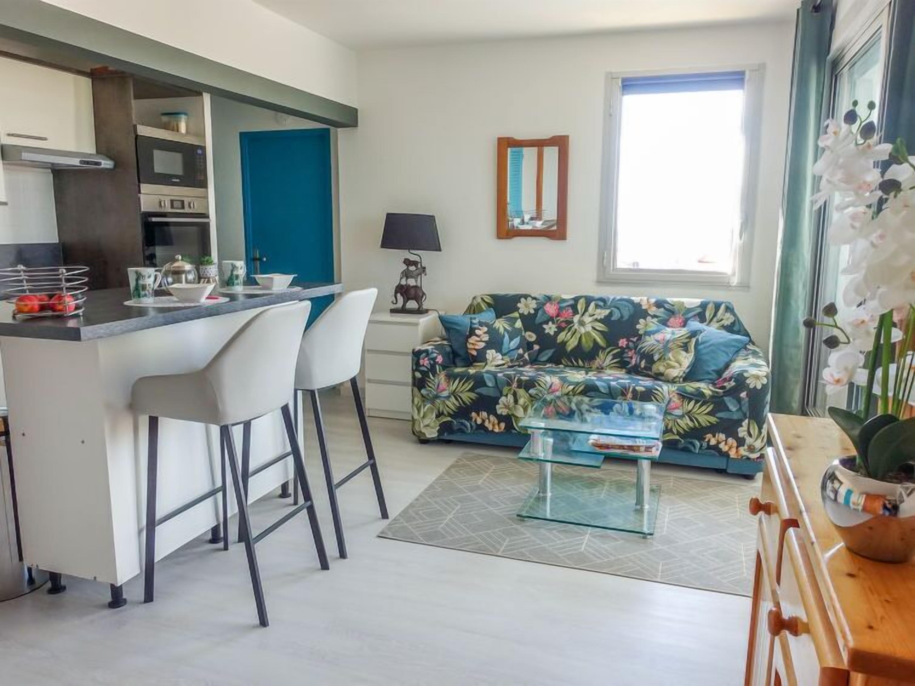 A modern kitchen with a central island, white bar stools, a floral sofa, and a small coffee table.