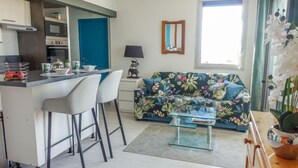 A modern kitchen with a central island, white bar stools, a floral sofa, and a small coffee table. - Apartment Estany by Interhome (Le Barcarès)
