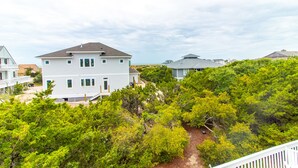 A white two-story house with a grey roof, surrounded by dense green trees. - Discover A Buena Vista on Bald Head Island with stunning views and island vibes. (Bald Head Island)