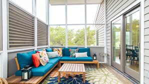 A covered porch with a blue sectional sofa, a wooden table, and a patterned rug. - Discover A Buena Vista on Bald Head Island with stunning views and island vibes. (Bald Head Island)