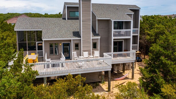 A two-story house with a balcony, a deck, and a small outdoor seating area. - Discover A Buena Vista on Bald Head Island with stunning views and island vibes. (Bald Head Island)