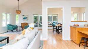 A spacious living room with a large gray sofa, teal chairs, and a wooden dining table. - Discover A Buena Vista on Bald Head Island with stunning views and island vibes. (Bald Head Island)