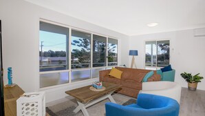 Ein modernes Wohnzimmer mit großen Fenstern, einem braunen Sofa, einem blauen Sessel und einem kleinen Holztisch.