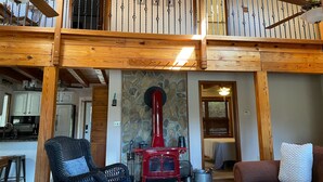 A spacious living area with a wooden balcony, a red wood stove, and a cozy seating arrangement.