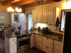 A kitchen with wooden cabinets, granite countertops, a stainless steel oven, and a dining area with a table and chairs.