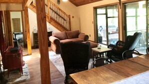 A spacious living area with a wooden ceiling, a staircase, a sofa, and a dining table.