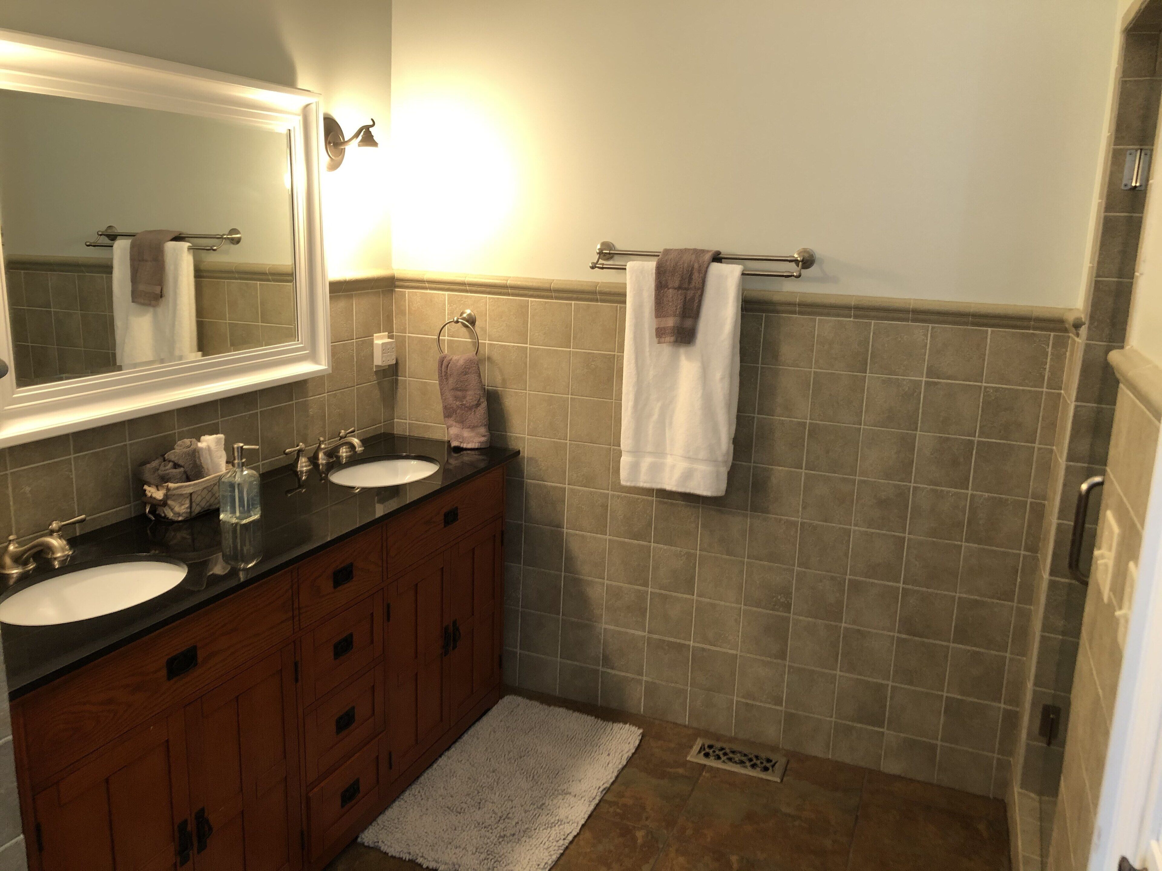 A bathroom with two sinks, a mirror, a towel rack, and a shower.