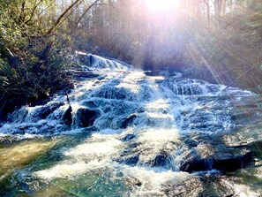A waterfall in a forested area with sunlight filtering through the trees.