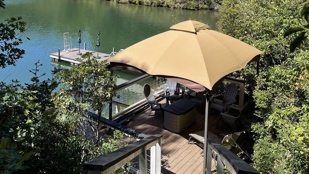 A deck with outdoor furniture and a canopy overlooking a lake, surrounded by dense greenery.