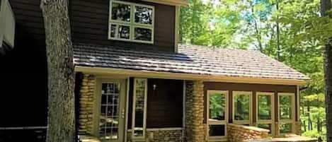 A two-story house with a stone exterior, large windows, and a covered patio area.