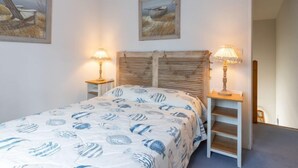 A bedroom with a bed, two bedside lamps, a wooden headboard, and two framed pictures on the wall.