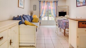 A cozy room with a white sofa, a dining table with a floral tablecloth, and a window with curtains.