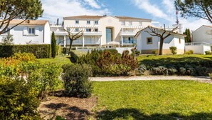 A residential building with multiple balconies, a well-maintained garden, and a clear blue sky.