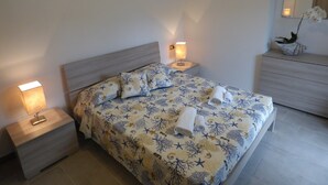 Una camera da letto ordinata con un letto, due comodini, un mobiletto, un quadro e una pianta in vaso.
