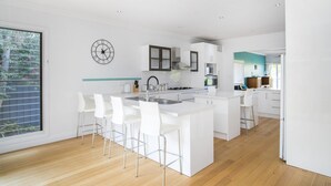 Une cuisine moderne avec des meubles blancs, un îlot central doté de tabourets de bar, un évier en acier inoxydable et une grande fenêtre donnant sur un paysage verdoyant.