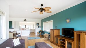 Un salon moderne comprenant un canapé, un pouf, un meuble pour la télévision et un ventilateur de plafond.