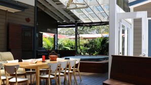Un espace repas à aire ouverte, avec une table et des chaises en bois, un banc et une vue sur la verdure grâce à de grandes fenêtres.