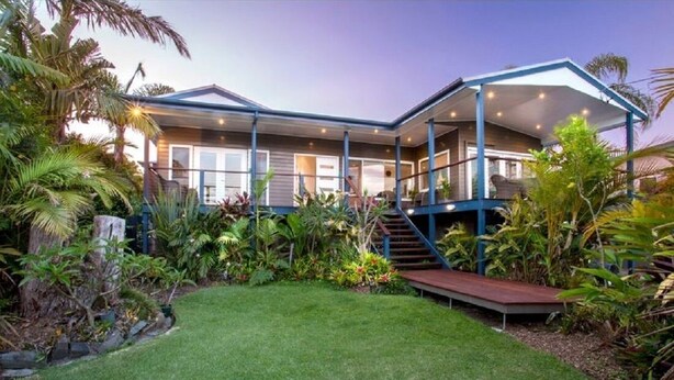 Une maison moderne dotée d’un porche abrité, d’une pelouse bien entretenue et de plantes tropicales.