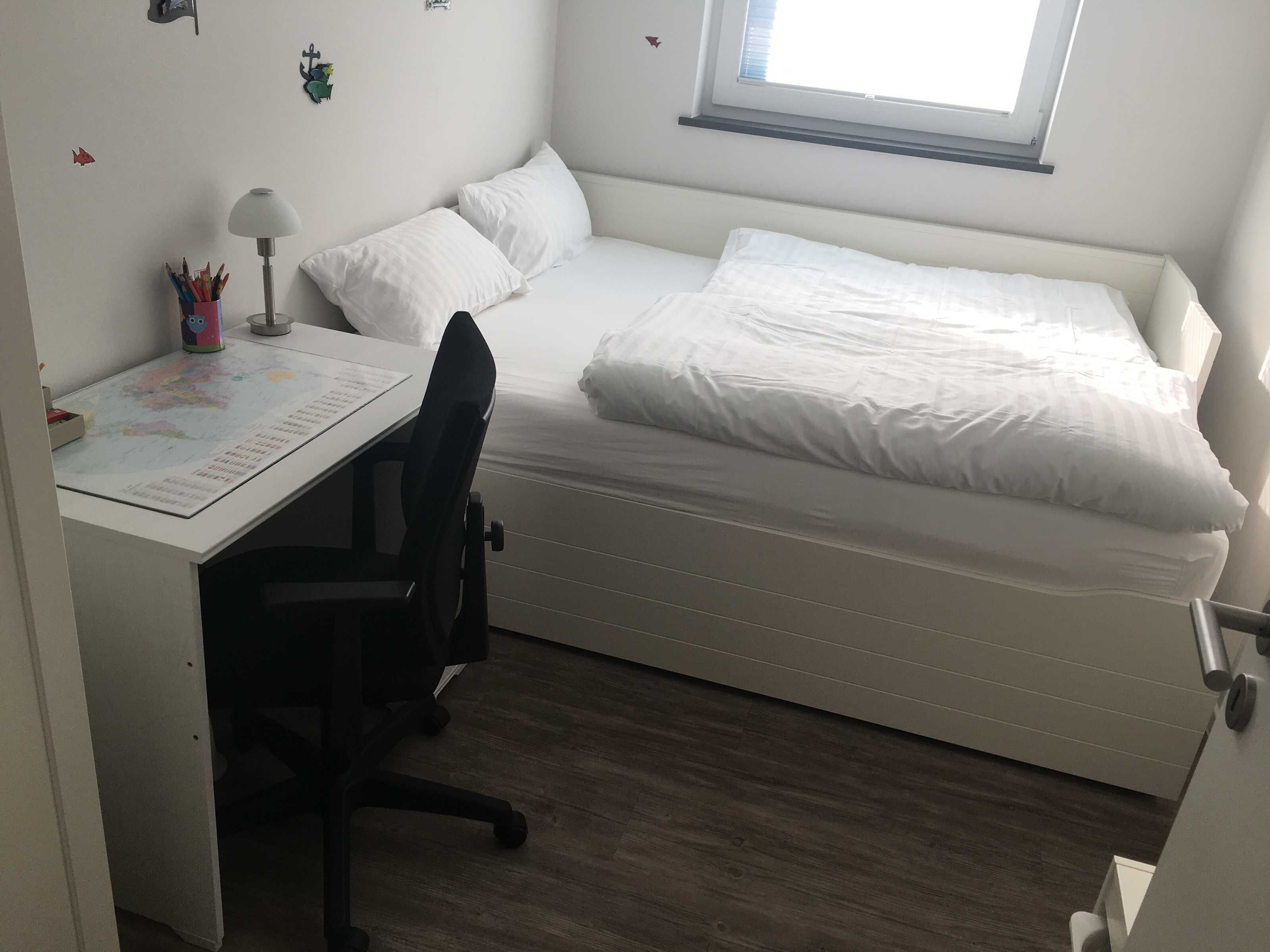 Een studentenkamer met een bed, bureau, stoel en raam.