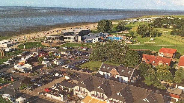 An aerial view of a coastal area with a parking lot, buildings, and a beach. - Papen, A. Ferienwohnung An Bord - An Bord (Varel)