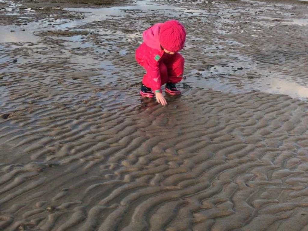 A child in a red outfit playing in wet sand.