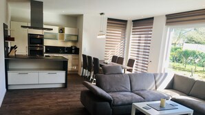 A modern living room with a grey sofa, a white coffee table, and a kitchen area with built-in appliances. - Papen, A. Ferienwohnung An Bord - An Bord (Varel)