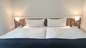 A neatly made bed with white linens and a dark-colored blanket, flanked by two wall-mounted lamps. - Papen, A. Ferienwohnung An Bord - An Bord (Varel)