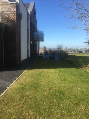 A building with a brick facade and a white exterior, a paved driveway, and a grassy area with outdoor seating. - Papen, A. Ferienwohnung An Bord - An Bord (Varel)