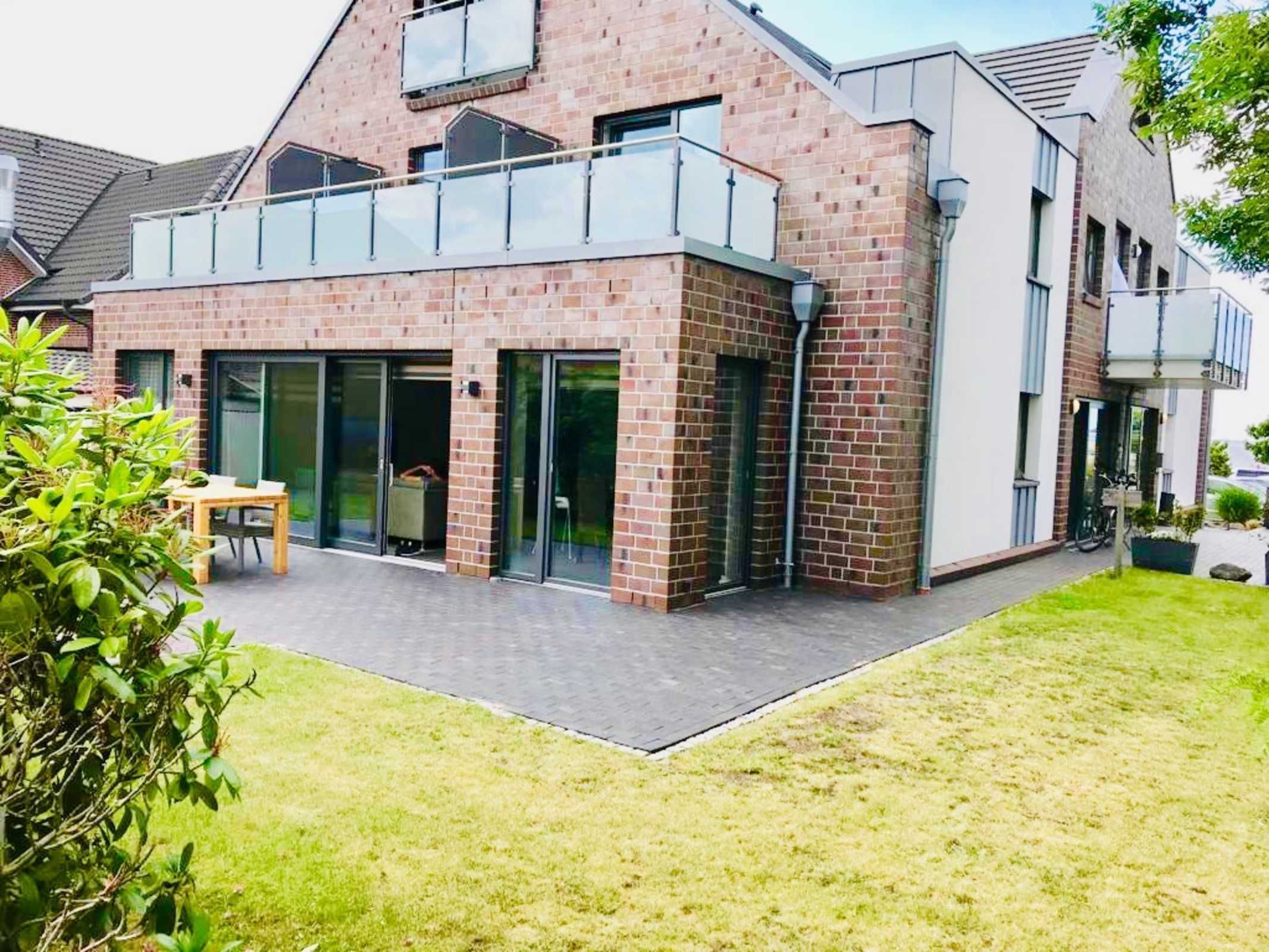 A modern house with a brick facade, large glass doors, and a balcony.