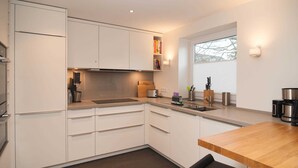 A modern kitchen with white cabinets, a wooden countertop, and a window providing natural light. - Mitte 6, Deutschland (Hörnum (Sylt))