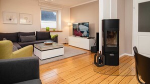 A modern living room with a sofa, coffee table, TV, and a wood-burning stove. - Mitte 6, Deutschland (Hörnum (Sylt))