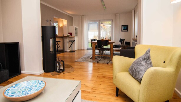 A modern living room with a yellow armchair, a glass coffee table, and a fireplace. There is a dining area with a table and chairs in the background. - Mitte 6, Deutschland (Hörnum (Sylt))