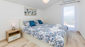 A bedroom with a bed, a nightstand, a lamp, a painting, and a window with a view. - Holiday house SAN MICHELE (Vrh)