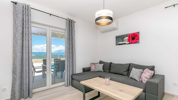 A modern living room with a grey sofa, a wooden coffee table, and a view of the sea through large glass doors. - Holiday house SAN MICHELE (Vrh)