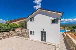 Uma casa de dois andares com uma parede de pedra e uma piscina ao fundo.