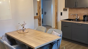 Une cuisine moderne avec une table à manger en bois, des chaises à revêtement gris et des luminaires suspendus.