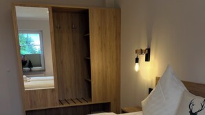 Une chambre d’hôtel avec un grand lit, une armoire en bois, un miroir et une table de chevet avec une lampe.