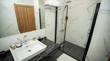 Un baño moderno con lavamanos de mármol, puerta de madera y ducha con mampara de vidrio.