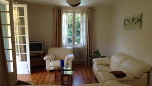 Ein Wohnzimmer mit einer Couch, einem Sessel und einem Fernseher auf einem Holzboden.