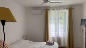 Ein Hotelzimmer mit einem Bett, einem Deckenventilator, einem Fernseher und einem Fenster mit Vorhängen.