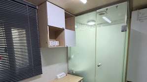 A compact hotel room with a desk, a small refrigerator, a glass-enclosed closet, and a bed. - Noble Residence (Seoul)