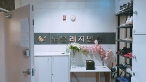 A reception area with a signboard, a desk with a vase of flowers, and a shoe rack. - Noble Residence (Seoul)
