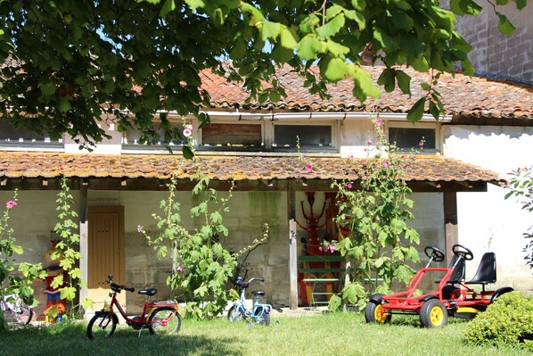 A building with a tiled roof, a porch, and a bicycle and a small red vehicle parked in front.