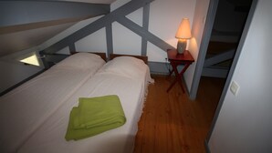 Ein Schlafzimmer mit einem Bett, einem grünen Handtuch, einem Nachttisch mit Lampe und Holzbalken an der Decke.