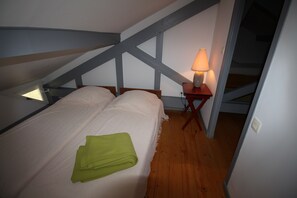 A bedroom with a bed, a green towel, a nightstand with a lamp, and wooden beams on the ceiling.