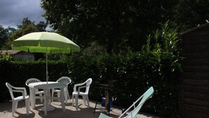 Ein Sitzbereich im Freien mit Tisch und Stühlen, einem grünen Sonnenschirm und einem Holzzaun.